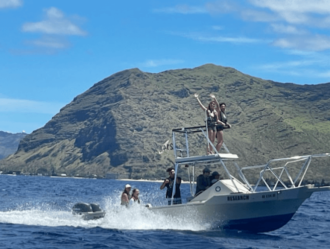 A group stands atop a small boat and wave towards the photographer.