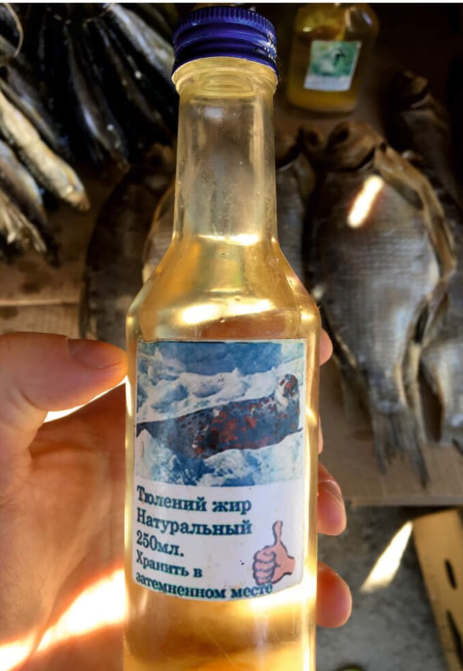 A small glass bottle with a sticker depicting a seal, filled with yellow liquid.